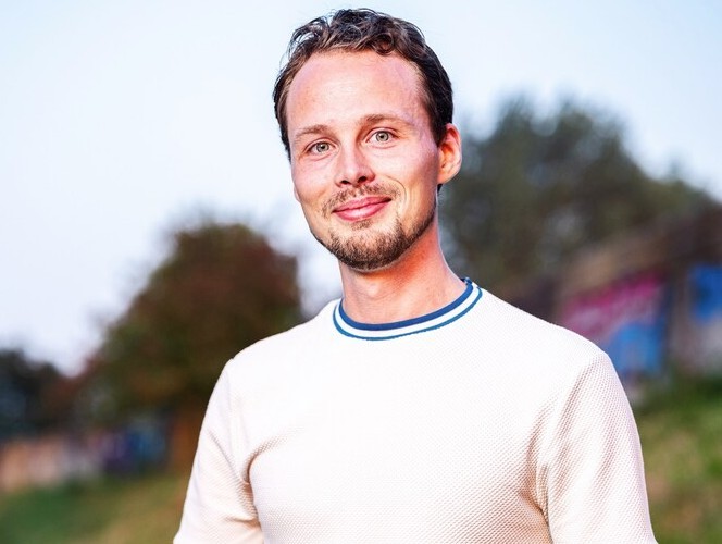 Man in wit shirt staand in een groen landschap.