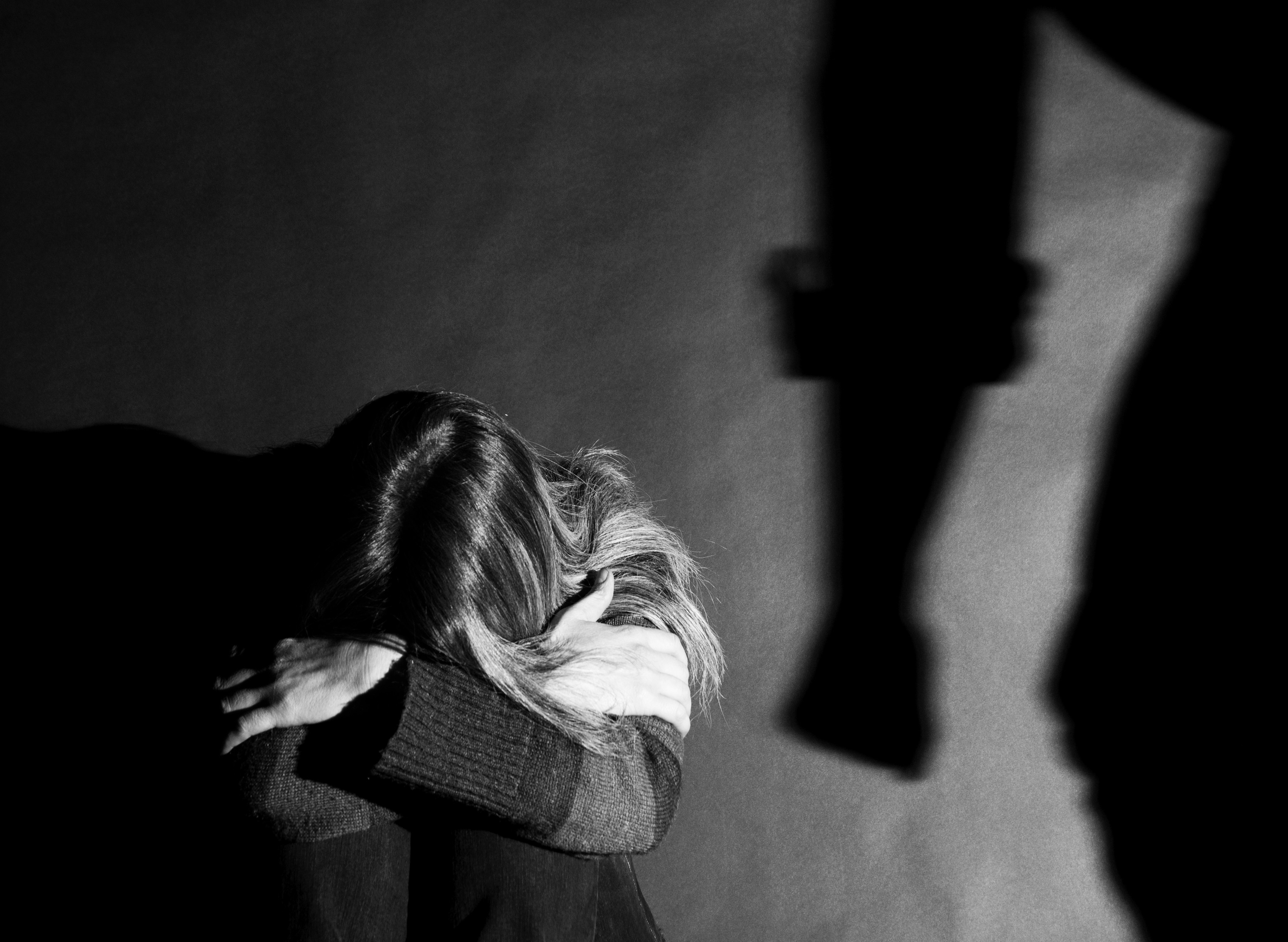 Donkere afbeelding van een vrouw met lange haren zittend op de grond met in de achtergrond een schaduw van een gebalde vuist.