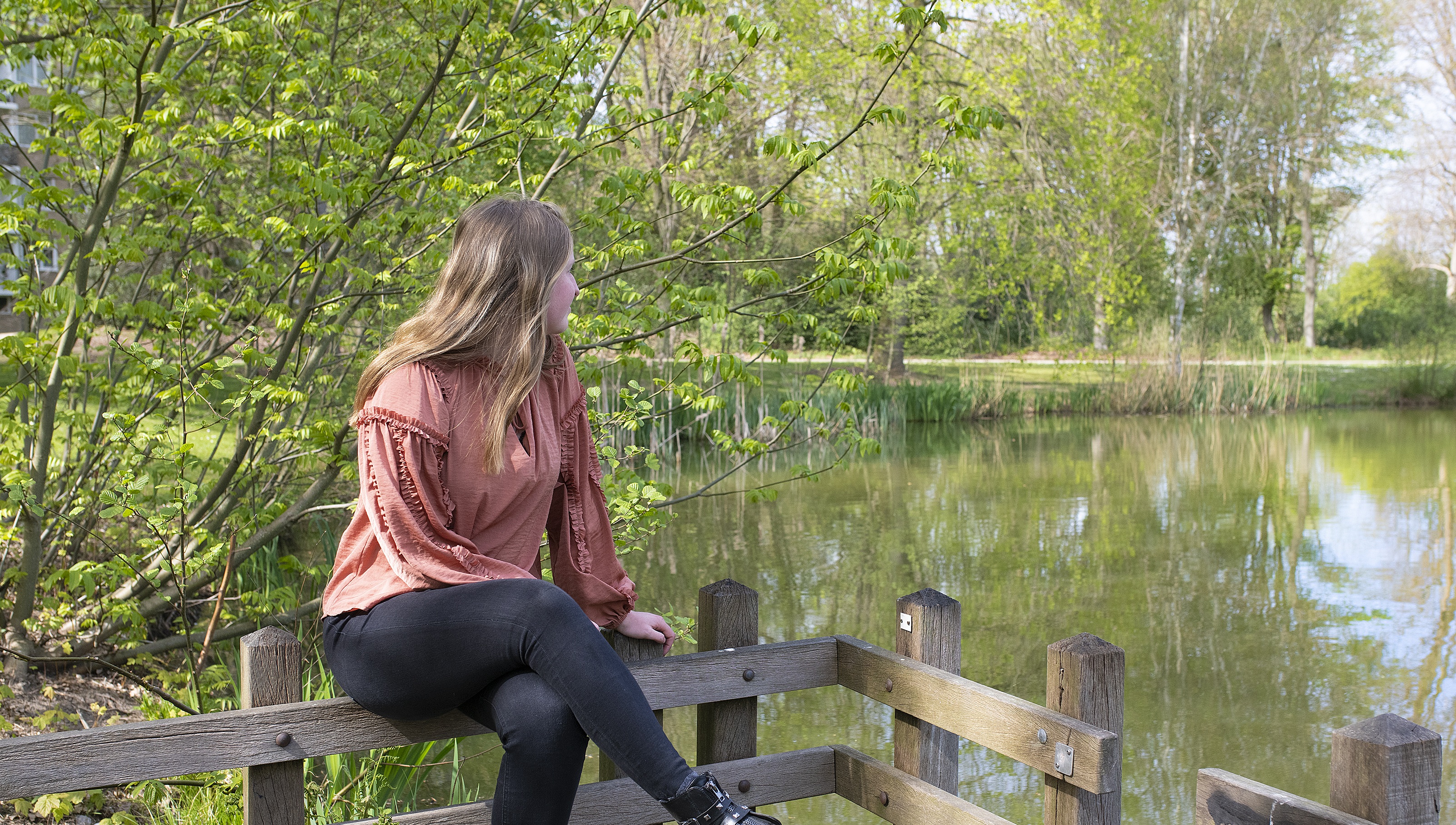 Vrouw zittend op een hekwerk en kijkt uit over een waterplas.